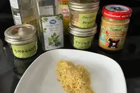 A grouping of spices to make homemade veggie bouillon and a sample of it on a white plate.