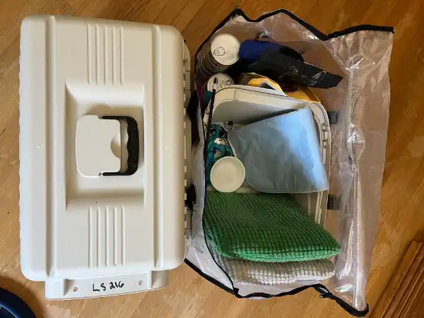 A photo of a cat carrier beside a cat disaster kit in a waterproof zippered bag that includes items like canned and dry food, litterbox/litter, bedding, dishes, harness and leash, toys.
